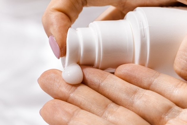 Hands holding a bottle with pink nails. 