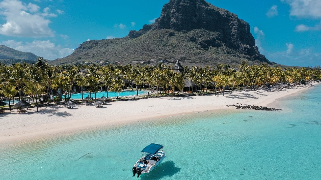 A boat travelling near the beach with a mountain in the background