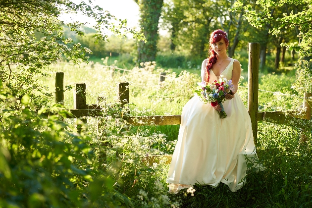 Bride sitting on fence in grounds of The Old Milking Parlour Cavokay House