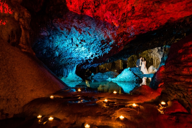 Wookey Hall Caves with bride and groom in background. Illuminated with red and blue lights